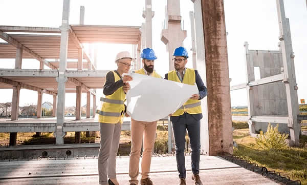3 people wearing hardhats reading a constuction drawing