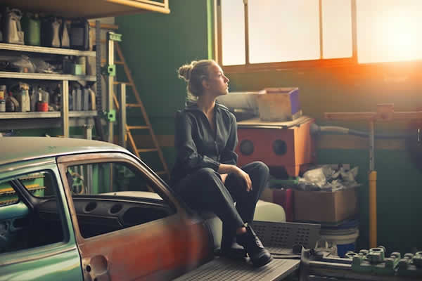 girl sitting on bumper of old car being restored in a garage