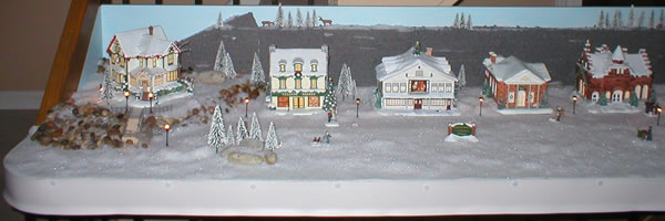 Christmas village finished shows house on raised deck, village bakery, studio, bank and city hall
