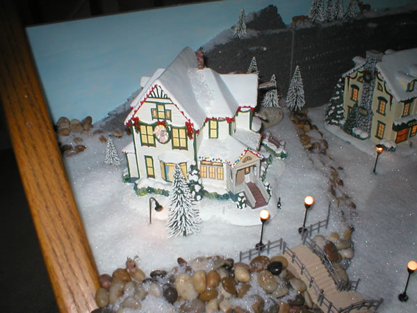 Christmas village finished shows house on raised deck, staircase, rocks and house lamppost lights