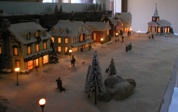 Christmas village finished shows front of church, boulders surrounded by pine trees, street lampposts and people