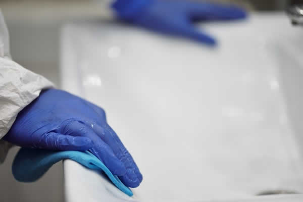 2 hands wearing blue gloves cleaning a white sink