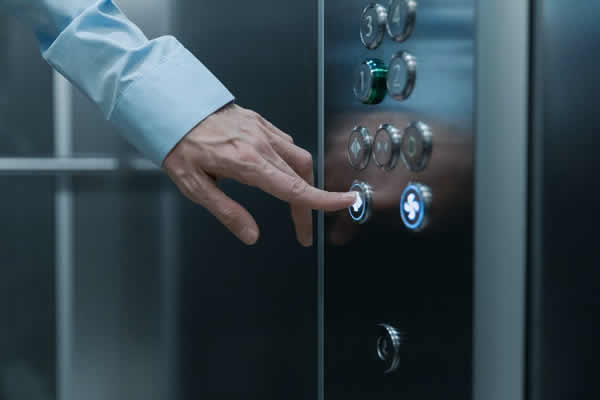 man in blue shirt pushing an elevator button to choose a floor
