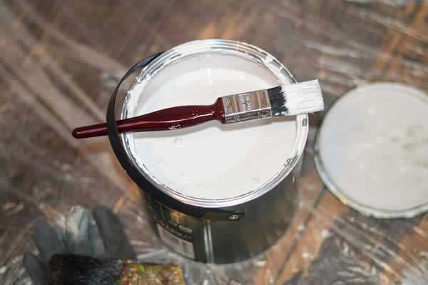 open gallon of white paint with brush lying on the top of the can
