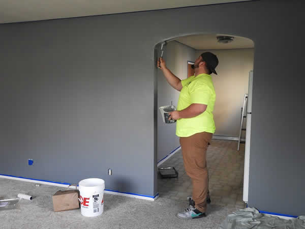man in yellow shirt painting a room grey