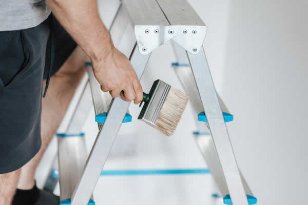 man climbing step ladder with a paint brush