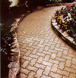 Winding walkway uses interlocking paving bricks against a stone retaining wall