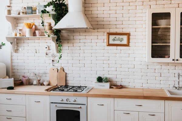 white kitchen with brick wall, gas stove and modern vent hood