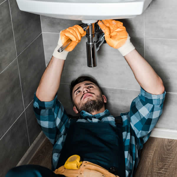plumber laying on back fixing a bathroom basin