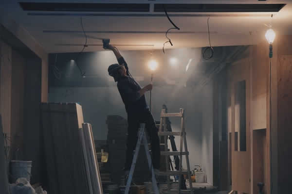 man working on ladder repairing ceiling