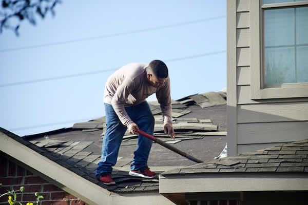 man scraping old asphalt shingles off roof