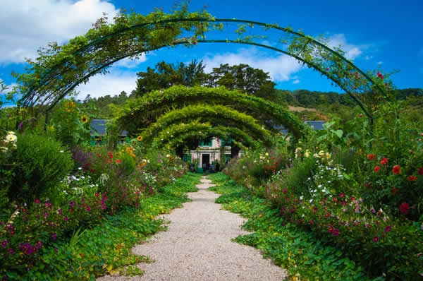 plant covered arches over a walkway leading to an old home
